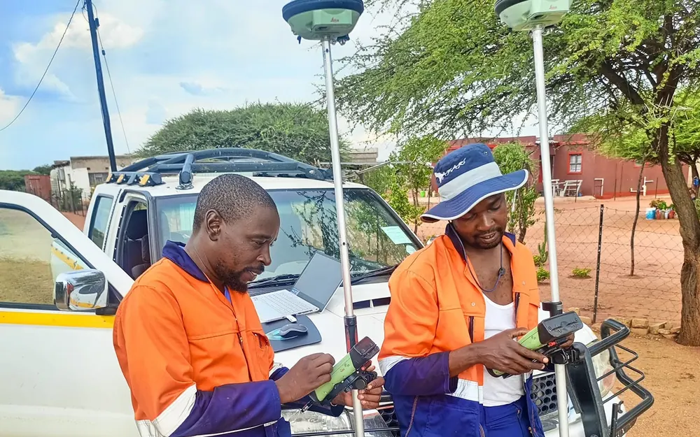 Two GeoSurv surveyors capturing points with GNSS receivers beside a company vehicle