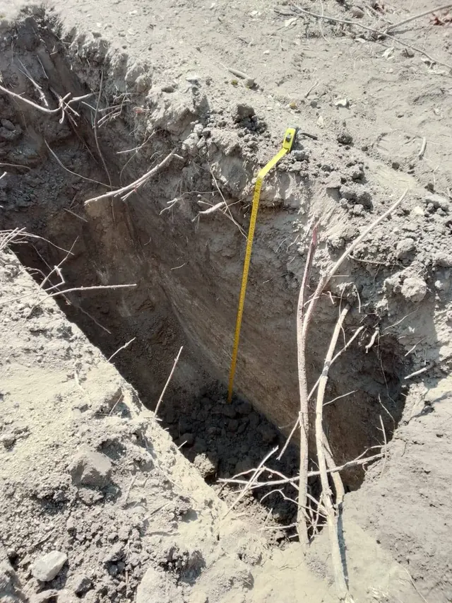 Deep test pit with a yellow measuring tape hanging into it